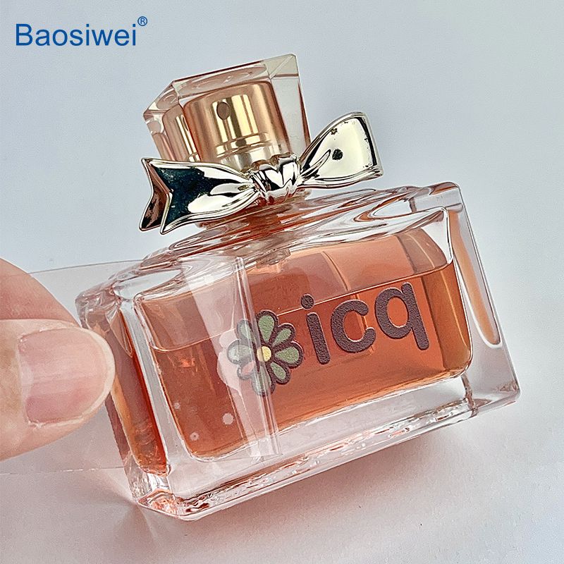 Crystal label printed with Baosiwei 30cm UV DTF printer being applied to a glass perfume bottle, showcasing delicate and precise transfer on curved surfaces.